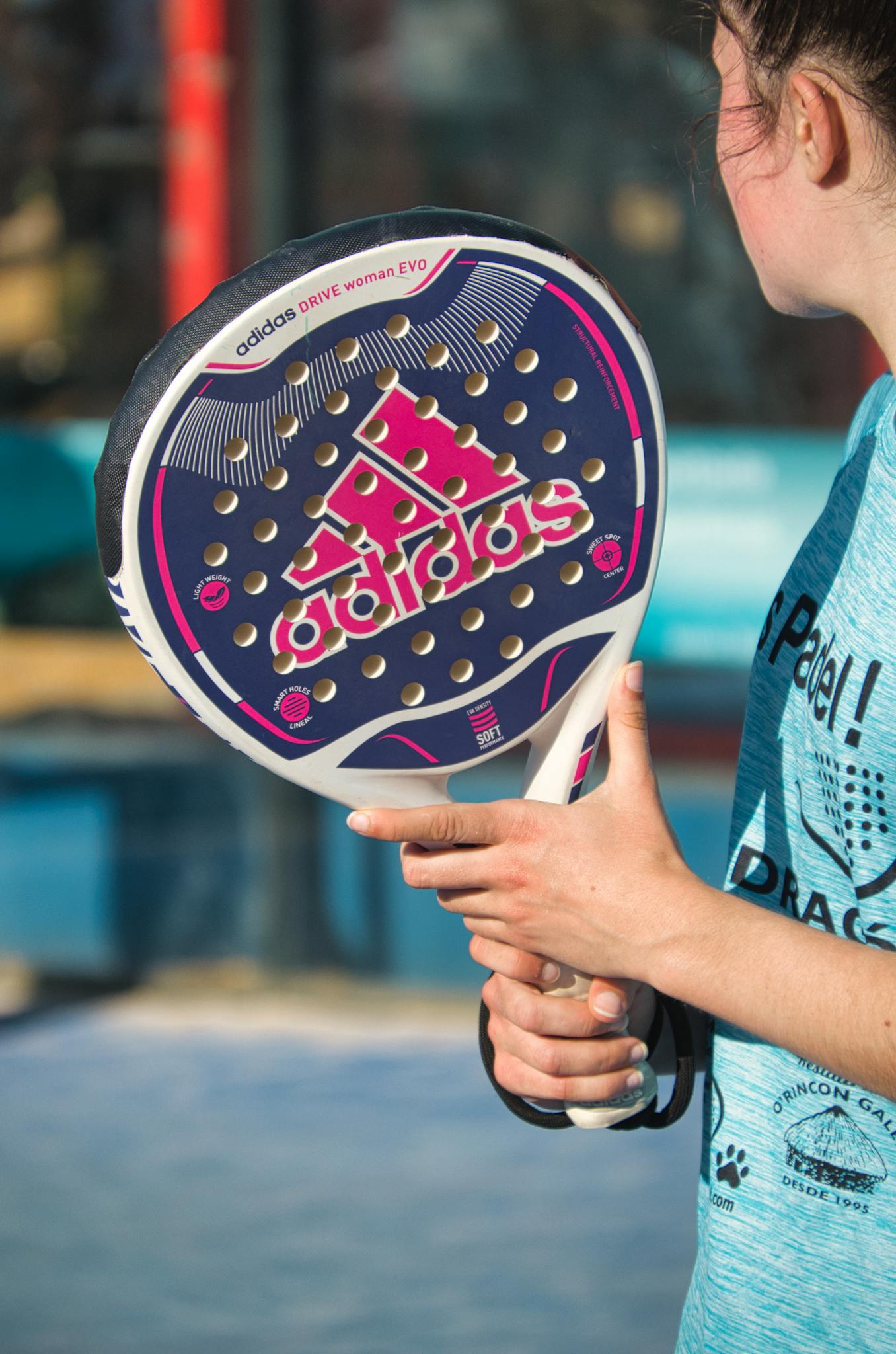 Woman playing padel outdoors with Adidas racquet, showcasing sports equipment in action.